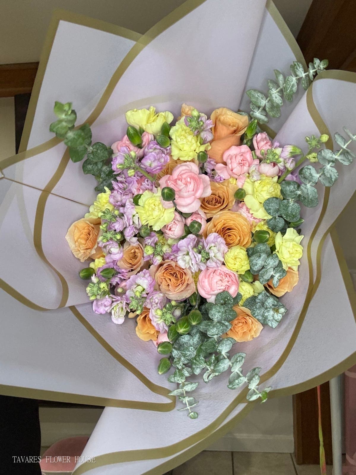 Wrapped custom bouquet of peach roses, pink and yellow carnations, lavender stock and eucalyptus