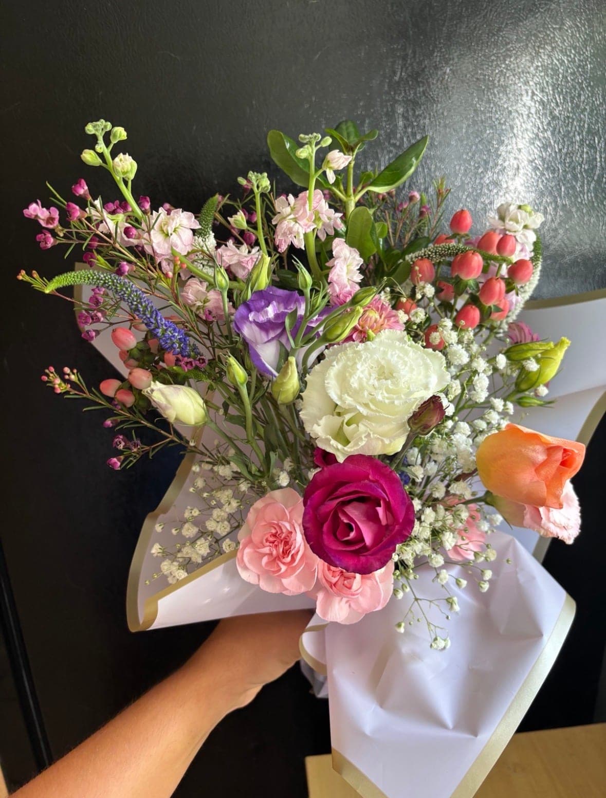 Garden-style bouquet with a magenta rose, purple lisianthus, a white carnation, pink stock and red hypericum berries