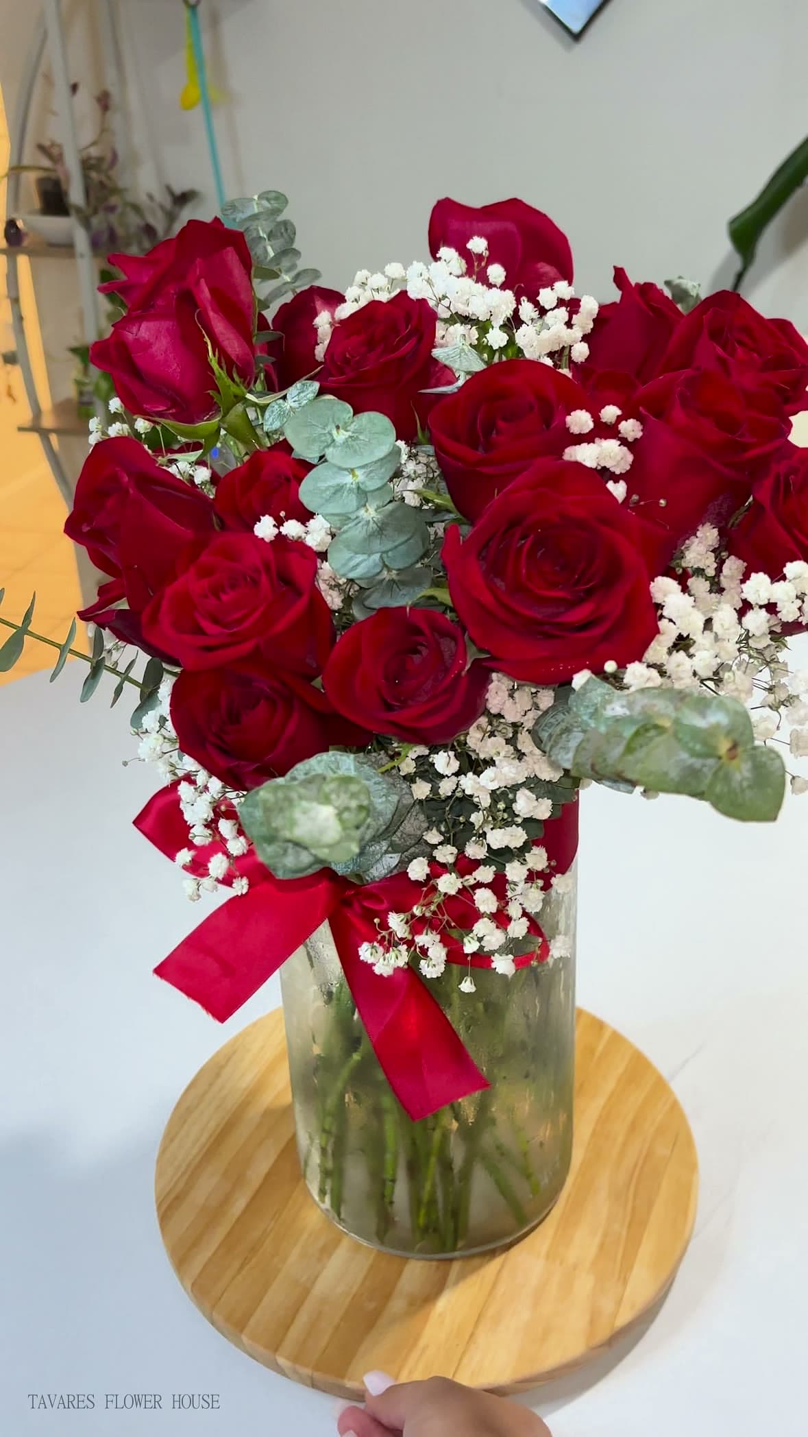 Two dozen red roses with baby's breath and eucalyptus in a glass vase, tied with a red ribbon